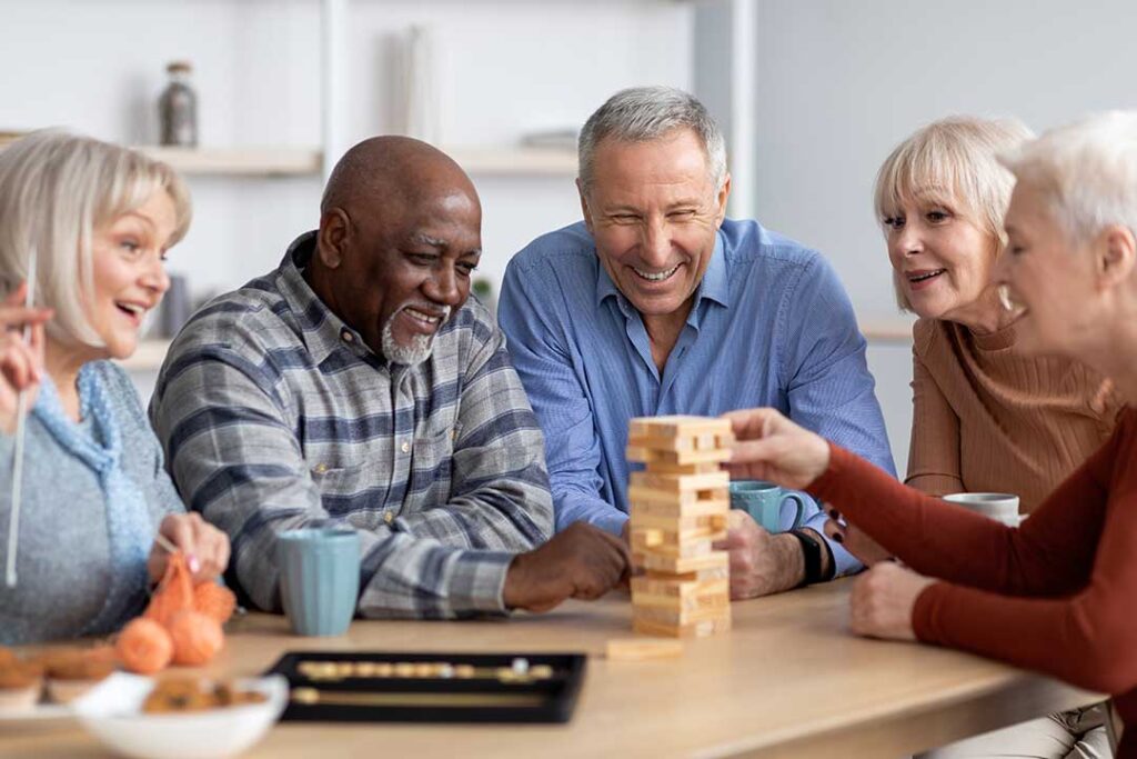 Older adults share a meal and conversation in a bright assisted living dining room.
